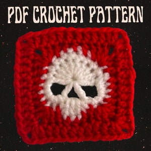 May include: A red crochet square with a white skull design in the center. The square is made with a single crochet stitch and has a textured look. The skull is made with a double crochet stitch and has a more open look. The background is a black sparkly fabric.