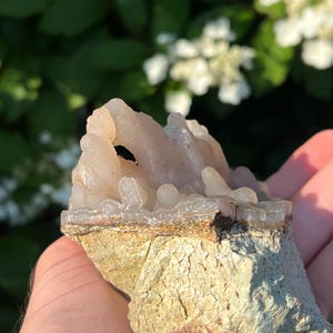 May include: A light-coloured, crystalline mineral specimen with a rough, textured base. The top portion features a cluster of translucent, rounded formations. The base is a mix of tan and green hues, with visible cracks and imperfections.