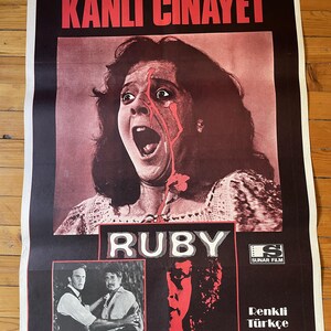 Könnte beinhalten: Ein Vintage-Filmplakat für den Film "Ruby" auf Türkisch. Das Plakat zeigt eine Frau mit Blut im Gesicht, die schreit. Der Text auf dem Plakat lautet "Kanli Cinayet", was im Deutschen "Blutiger Mord" bedeutet. Das Plakat zeigt auch die Namen der Schauspieler Piper Laurie und Stuart Whitman sowie des Regisseurs Curtis Harrington.