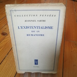May include: A white book with blue text on the cover. The title is "L'EXISTENTIALISME EST UN HUMANISME" and the author is "JEAN-PAUL SARTRE". The book is part of the "COLLECTION PENSÉES" series.