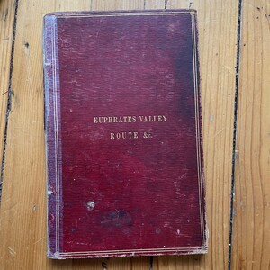 May include: A red, worn book with gold lettering on the cover. The title reads "Euphrates Valley Route & Co."
