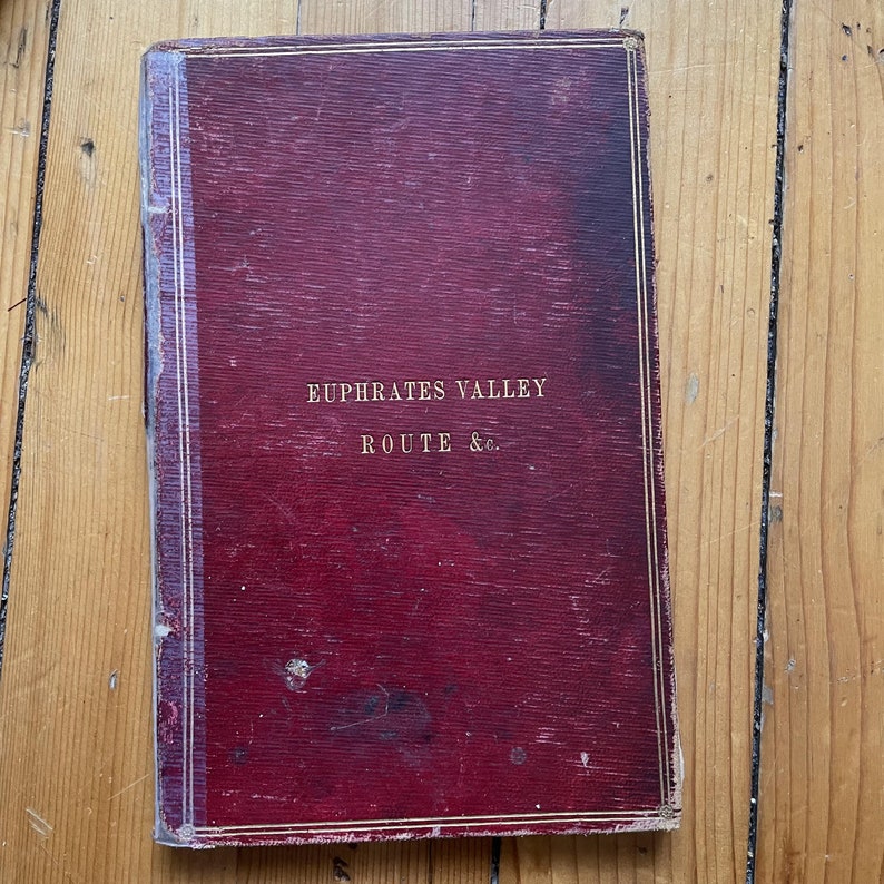 May include: A red, worn book with gold lettering on the cover. The title reads "Euphrates Valley Route & Co."