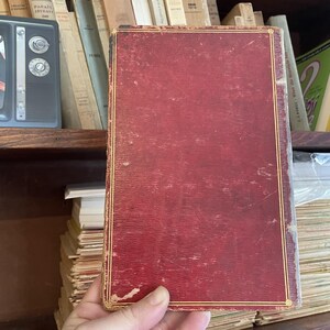 May include: A red hardcover book with gold trim and a worn, textured surface.
