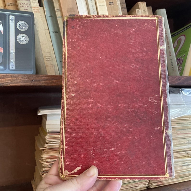 May include: A red hardcover book with gold trim and a worn, textured surface.
