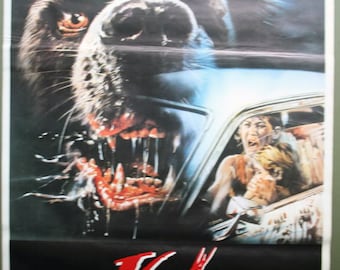 May include: Movie poster for "Cujo" featuring a menacing, snarling dog with exposed teeth and blood. A car with terrified occupants is visible. The title "Cujo" is in red, with the names of the actors below.