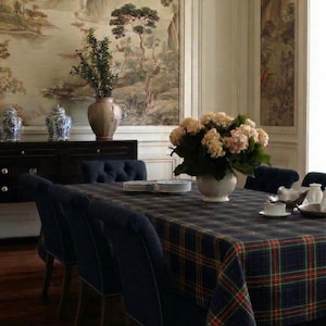 May include: A dining room scene featuring a dark wood table set with a plaid tablecloth in navy, red, and green. Navy blue upholstered chairs surround the table. A large vase of flowers sits in the center. The room has a scenic mural on the wall.