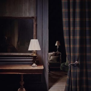 Puede incluir: Una cortina de cuerpo entero con un patr&oacute;n de cuadros en verde oscuro, azul marino y naranja, sujeta por un alzapa&ntilde;os de metal decorativo. La cortina cuelga junto a una mesa consola de madera con una l&aacute;mpara de pantalla plisada y un espejo.