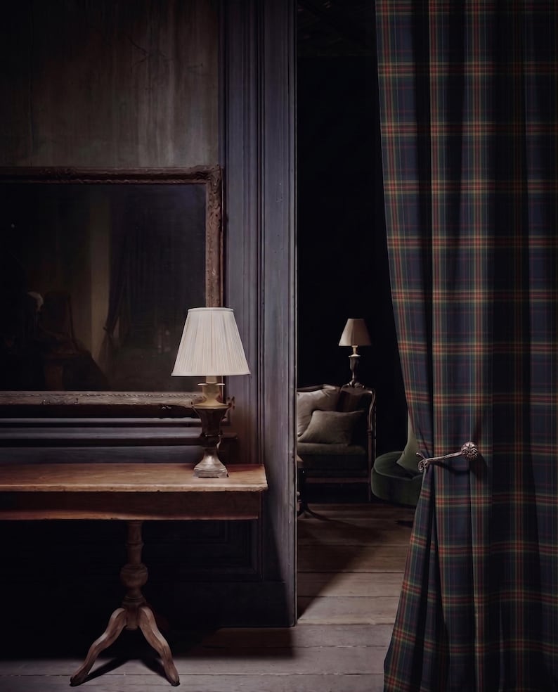 Puede incluir: Una cortina de cuerpo entero con un patr&oacute;n de cuadros en verde oscuro, azul marino y naranja, sujeta por un alzapa&ntilde;os de metal decorativo. La cortina cuelga junto a una mesa consola de madera con una l&aacute;mpara de pantalla plisada y un espejo.