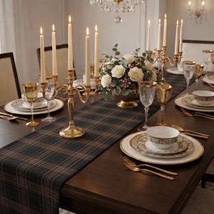 May include: A formal dining table setting featuring a dark green and brown plaid table runner, gold candelabras with cream taper candles, white floral centerpieces, gold-rimmed plates, patterned bowls, and gold-toned cutlery and glassware.