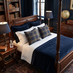 K&ouml;nnte beinhalten: Ein Himmelbett mit einer marineblauen Samtdecke und Kissen. Das Bett ist mit wei&szlig;en Laken und karierten Akzentkissen bezogen. Zwei Lampen mit marineblauen Schirmen stehen auf den Nachttischen. Eine Weltkugel und eine Kommode sind im Hintergrund zu sehen.