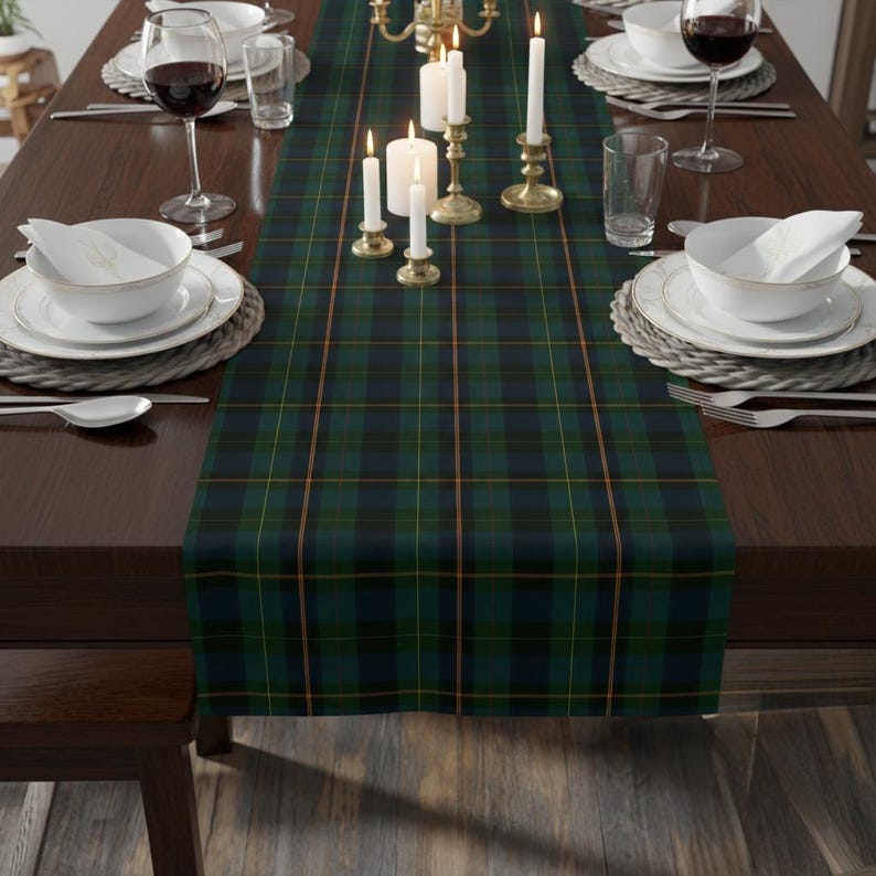May include: A dark green and navy blue plaid table runner with thin gold lines. The runner is on a dark brown wooden table set for a formal dinner. White candles in gold candle holders and white dishes are visible.