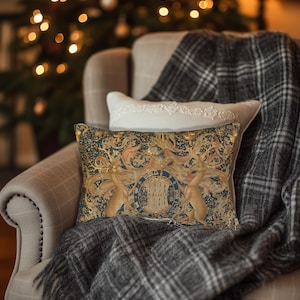 May include: A throw pillow with a tapestry design featuring two golden deer and a crest with the text "Honi Soit Qui Mal Y Pense". The pillow is on a gray and white plaid throw blanket in a plush armchair.
