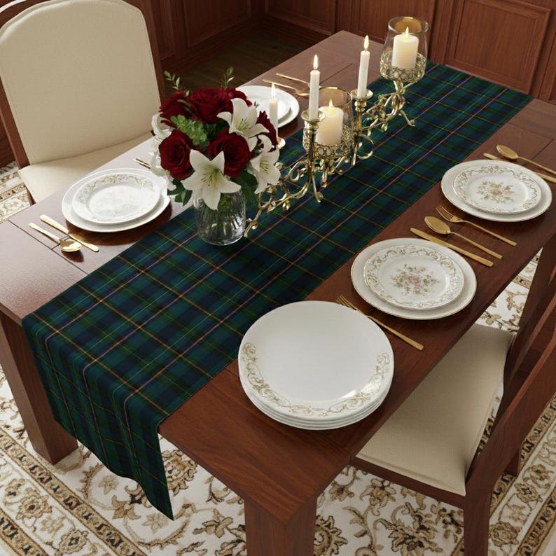May include: A dining table set for a formal occasion. The table features a green and navy plaid table runner, white plates with gold rims, gold silverware, and a floral centerpiece. Lit candles in gold holders add ambiance.
