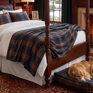 Puede incluir: Una manta a cuadros de color verde oscuro, azul marino y rojo colocada sobre una colcha blanca en una cama con dosel de madera. Una cama para perros a cuadros a juego con un golden retriever durmiendo está en el suelo junto a la cama.