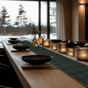 May include: A dining table set for a meal, featuring black bowls, chopsticks, and a green plaid table runner. Lit candles in glass holders and a vase with dried flowers add ambiance. The table is set near a large window.