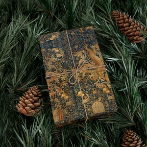 May include: A wrapped gift with a detailed, ornate pattern in navy blue and gold, tied with twine. The design features architectural elements and a deer. The gift is surrounded by green pine needles and pine cones, suggesting a holiday theme.