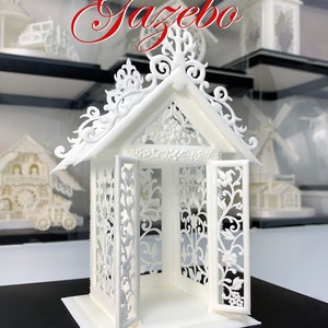 May include: A white sugar art gazebo with intricate details and open doors. The gazebo is made of royal icing and is decorated with delicate floral patterns. The text "Royal Icing Gazebo" is written in red above the gazebo. The text "Vinism Sugar Art" is written below the gazebo.