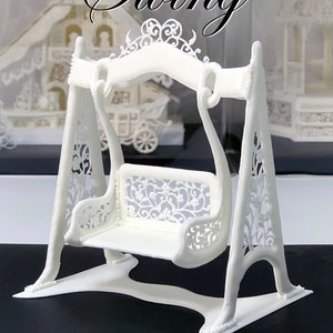 Può includere: Un'altalena di zucchero bianco con dettagli intricati, realizzata con glassa reale. L'altalena è su una superficie nera con il testo "Vinism Sugar Art" sotto. Il testo "Royal Icing Swing" è in alto nell'immagine.