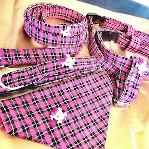 May include: Pink and black plaid dog collar, harness, and bandana set with skull-shaped charms.