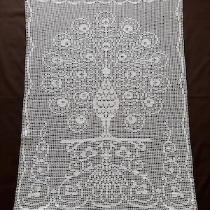 Puede incluir: Tapete rectangular blanco de ganchillo con un diseño de pavo real. El cuerpo del pavo real está en la base, con una larga cola adornada que se abre hacia arriba. Los bordes tienen un borde decorativo. El tapete está hecho de un tejido fino y abierto. Aproximadamente 50 cm x 70 cm.