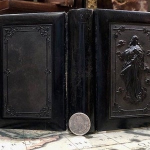 May include: A black leather-bound book with a raised image of a woman on the front cover. The book is closed and has a silver clasp.