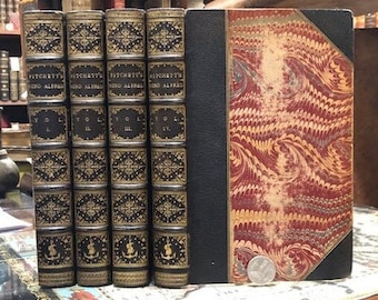 May include: Set of four antique books with black and gold covers. The books are titled "Hitchin's Nino Alfred" and each volume is numbered I through IV. The books are bound in leather with marbled paper covers.
