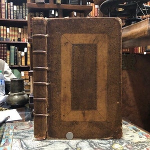 May include: A large, antique, brown leather-bound book with a decorative border and a worn, aged appearance.