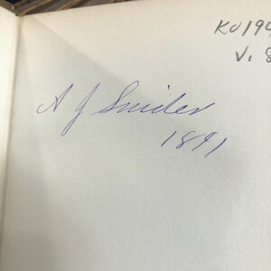 May include: A close-up of a book page with a handwritten signature in blue ink. The signature reads "A. J. Smiler" above the year "1891". The upper right corner has additional handwritten text.