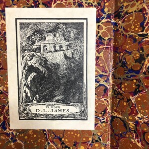 May include: A black and white bookplate featuring a detailed illustration of a building on a cliffside, with the text "EX LIBRIS D.L. JAMES" at the bottom. The bookplate is set against a marbled paper background.