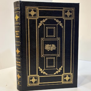 May include: A black hardcover book with gold foil stamping on the front cover and spine. The spine reads "Ninety-Five Theses" and "Martin Luther" with Celtic cross icons. The front cover features a central eagle emblem and geometric borders.