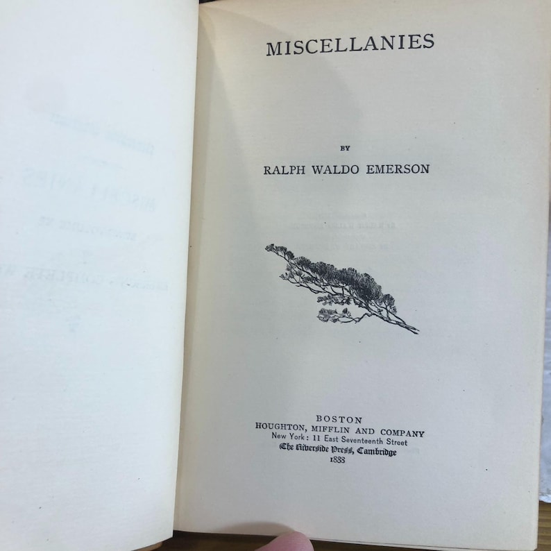 May include: Open book with the title "MISCELLANIES" by Ralph Waldo Emerson. The page features a black and white illustration of a plant and the publisher's information: Houghton, Mifflin and Company, Boston, New York, and Cambridge, 1883.
