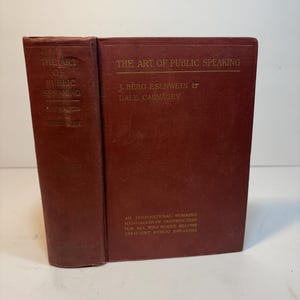 May include: A vintage, maroon-colored book titled "The Art of Public Speaking" by J. Berg Esenwein and Dale Carnegie. The book's spine and cover feature gold lettering. The book is a handbook of instruction for efficient public speakers.