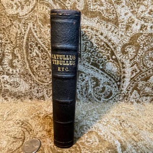 May include: A black leather-bound book with gold lettering on the spine that reads "Catullus Tibullus Etc."