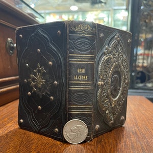 May include: A vintage leather-bound book with gold and silver embellishments. The title on the spine reads "GESU AL CUORE".