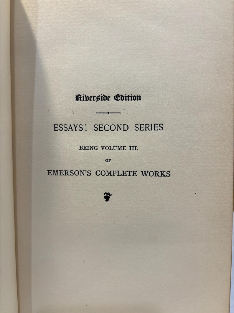 May include: Open book page with text: "Riverside Edition," "Essays: Second Series," "Being Volume III," and "Emerson's Complete Works." The text is in black ink on a cream-colored paper.