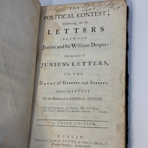 May include: An antique book titled The Political Contest, containing letters between Junius and Sir William Draper. The off-white page features black printed text, handwritten ink notes at the top, and visible age-related paper discoloration.