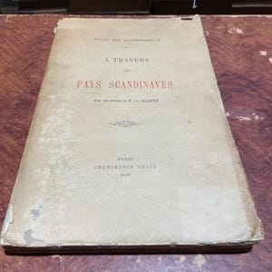 May include: A vintage book titled "A Travers Les Pays Scandinaves" by Henri de Rothschild, with a preface by M. de Claretie. The book was published in Paris by Imprimerie Chaix in 1890.
