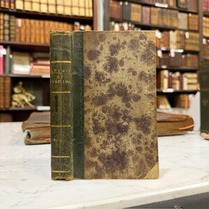 May include: An antique book with a worn, mottled cover in shades of tan and brown. The spine is dark green with gold lettering that reads "Spirit of Partridge." The book is displayed in a library setting, suggesting a vintage or historical theme.