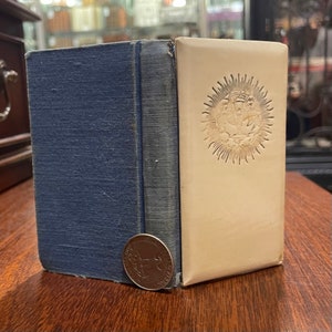 May include: A blue hardcover book with a white embossed design on the front cover. The design features a sun with a stylized image of a bird inside.