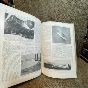 Puede incluir: Una fotograf&iacute;a en blanco y negro de un libro antiguo sobre aviaci&oacute;n. El libro est&aacute; abierto en una p&aacute;gina con una foto de un gran portaaviones y un avi&oacute;n m&aacute;s peque&ntilde;o. El texto en la p&aacute;gina dice "Aerial Age".