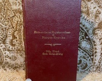 May include: A burgundy leather-bound book with gold lettering on the spine. The title is "Helnordens Rigskroniker * Norges Kronika" and the author is "Nik. Fred. Sev. Grundtvig".