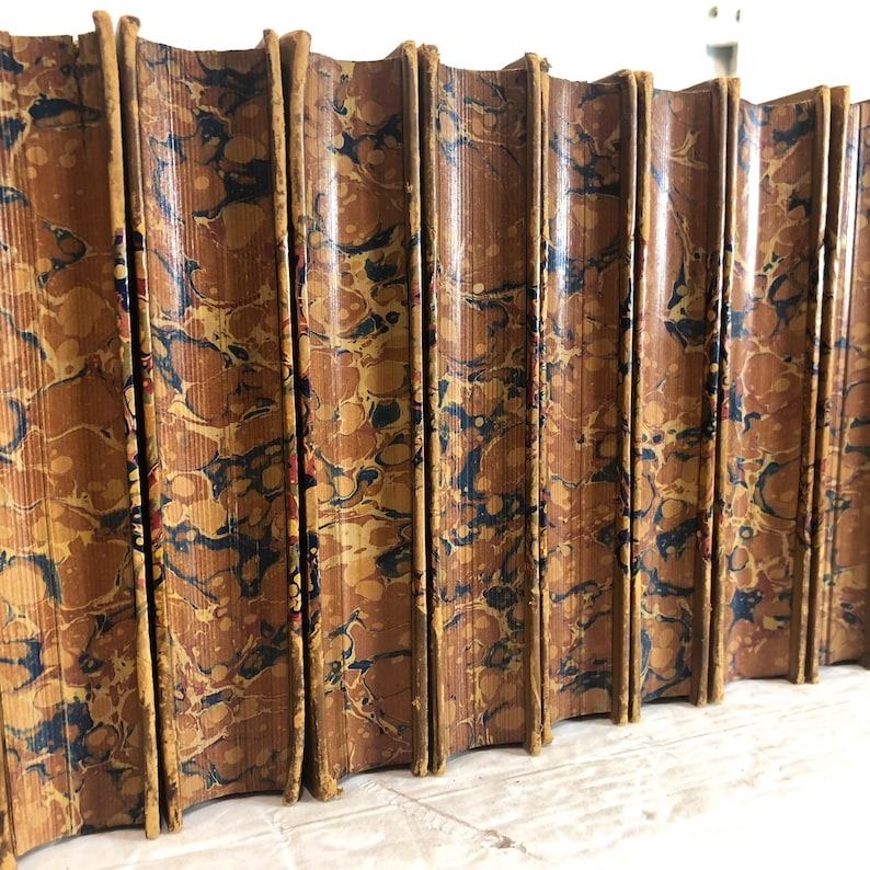 May include: A row of antique books with marbled covers. The covers are a mix of brown, blue, and gold, with a textured, swirling pattern. The spines are rounded and show signs of age.