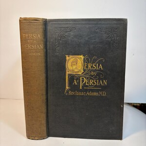 May include: An antique book titled "Persia by a Persian" with a dark cover and gold lettering. The spine is a lighter brown color. The book is standing upright.