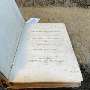 May include: A vintage book titled "Oliver Twist, or The Parish Boy's Progress" by Box. The book was published in Philadelphia by Carey, Lea and Blanchard in 1837.