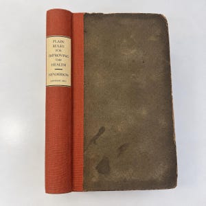 May include: An antique hardcover book with a textured orange spine and a dark, weathered gray cover. The spine features a white label with black text reading: Plain Rules for Improving the Health, Henderson, London, 1831. The edges show wear.