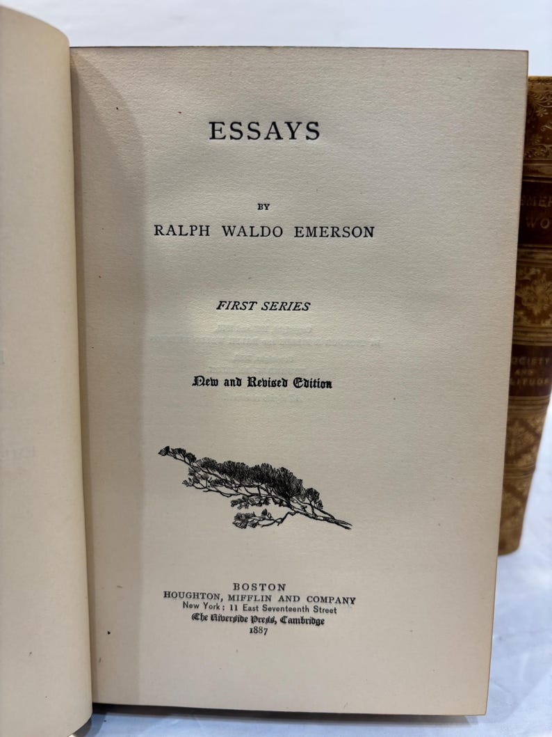 May include: Open book with the title "ESSAYS" by Ralph Waldo Emerson. The cover is off-white with black text and a small illustration. The book is a "New and Revised Edition" published in Boston in 1887.