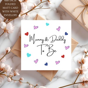 May include: A 15.24 x 15.24 cm square folded matte greeting card with a white envelope. The card features the black text Mummy & Daddy To Be in the centre, surrounded by small hand-drawn hearts in red, pink, light blue, and dark blue colours.