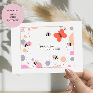 May include: A white folded card with a thank you message and a cute bee and butterfly design. The card has a pink, orange, and purple polka dot pattern.
