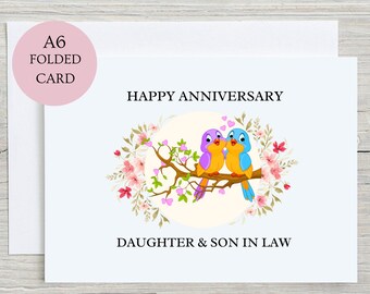 May include: A6 folded card with a white envelope. The card features the text "HAPPY ANNIVERSARY" and "DAUGHTER & SON IN LAW". It has a floral design with two cartoon birds on a branch. The birds are purple, yellow, and blue.
