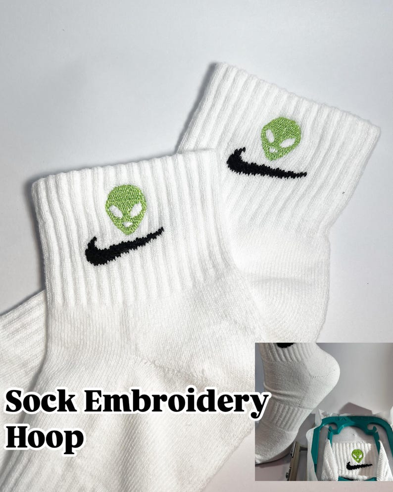 Pu&ograve; includere: Calzini bianchi alla caviglia con un swoosh Nike nero e un ricamo di alieno verde. I calzini sono in un cerchio da ricamo, con il testo "Sock Embroidery Hoop" sotto.